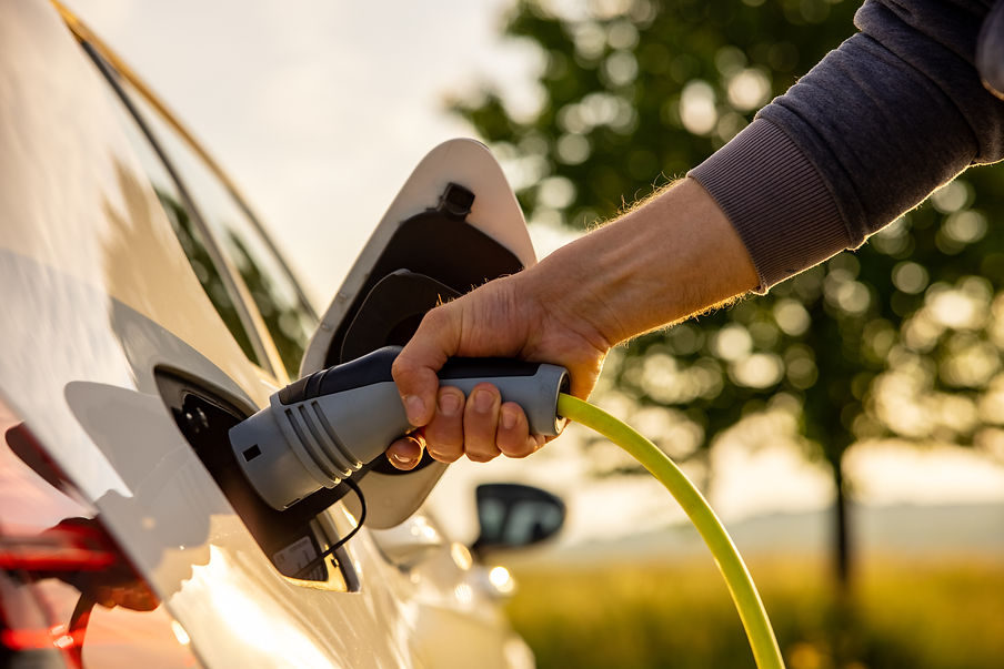 Hand of man inserting a power cord into an electric car for charging ecofriendly vehicle o
