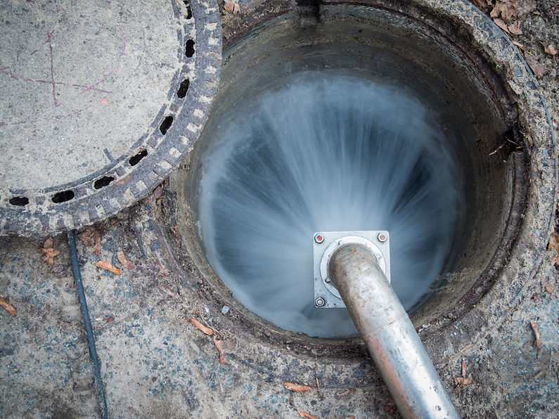 Close-up of a water jet from a metallic pipe into a circular storm drain
