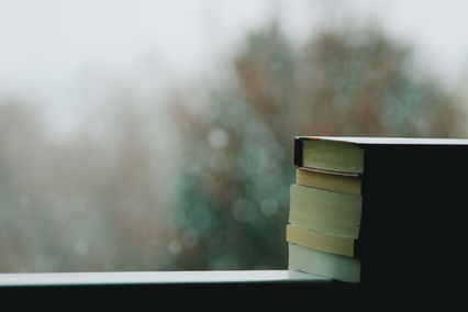 Stack of books by a window, with a soft blurred outdoor background and a calm, quiet mood.
