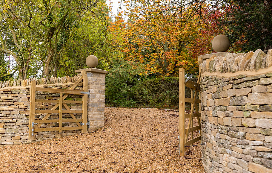 Stylish wooden gates across gravel drive and cotswold stone wall