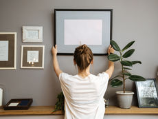  Arranging a gallery wall: a person carefully hangs a large picture frame, adding to the stylish decor in a cozy room.