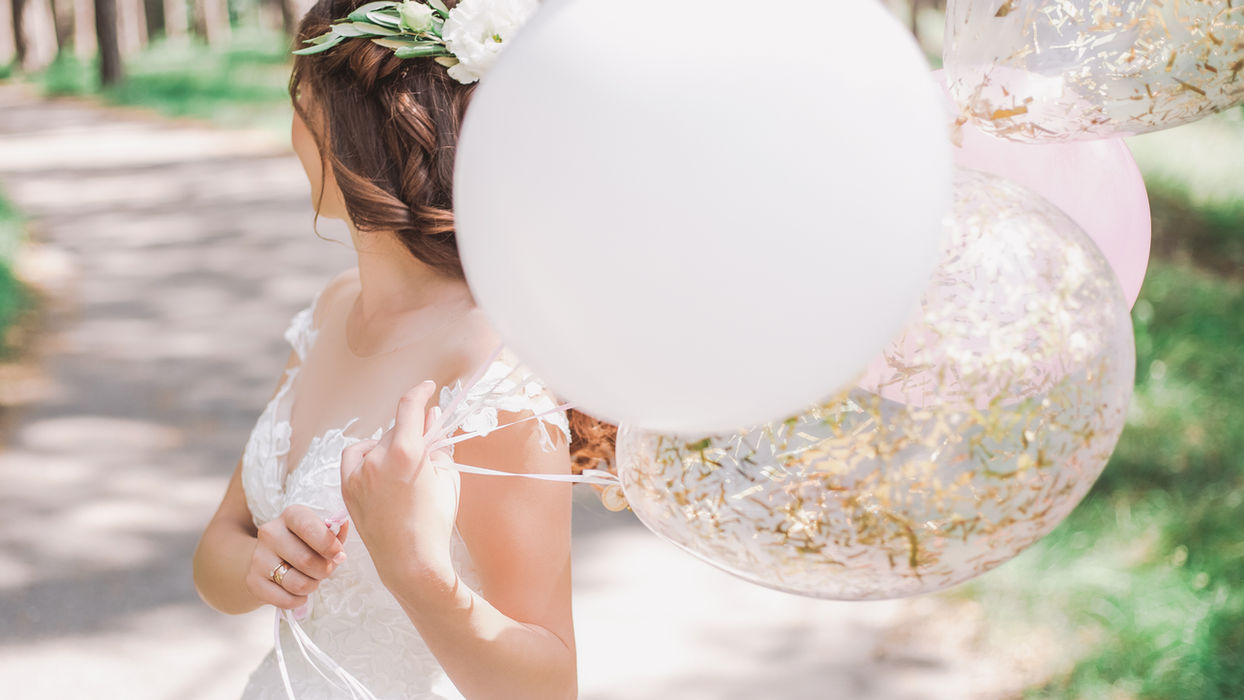 bride wearing a lace whimscal wedding dress holding balloons.