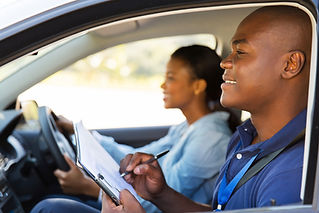 A driving instructor with a clipboard is teaching a female student