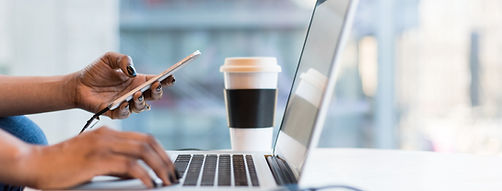 An individual multitasking, using a computer and holding a phone.