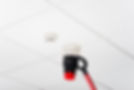 Fire alarm on white ceiling tested with red and black tool
