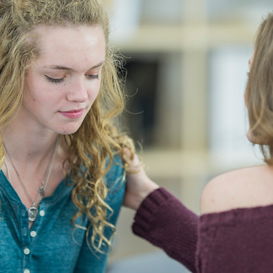 A close-up view showing a blonde therapist placing a supportive hand on a young client's shoulder