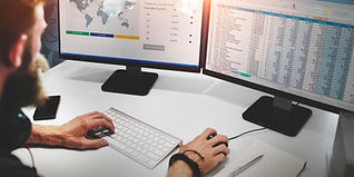 A Man is working with dual monitors showing graphs and data
