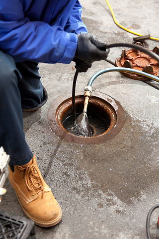 Gloved hands feeding a professional CCTV drainage inspection camera into an open circular manhole