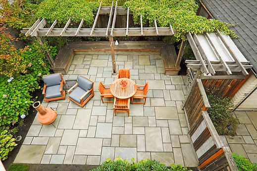 Aerial view of a stone patio with outdoor dining furniture beneath a wooden pergola