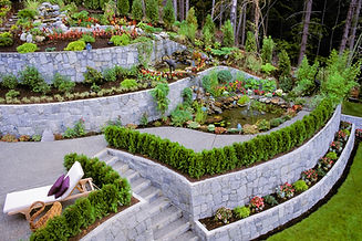 A garden with stone retaining walls, ponds and vibrant flower beds