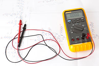 Yellow digital multitester tool with red and black probes on an electronic scheme diagram