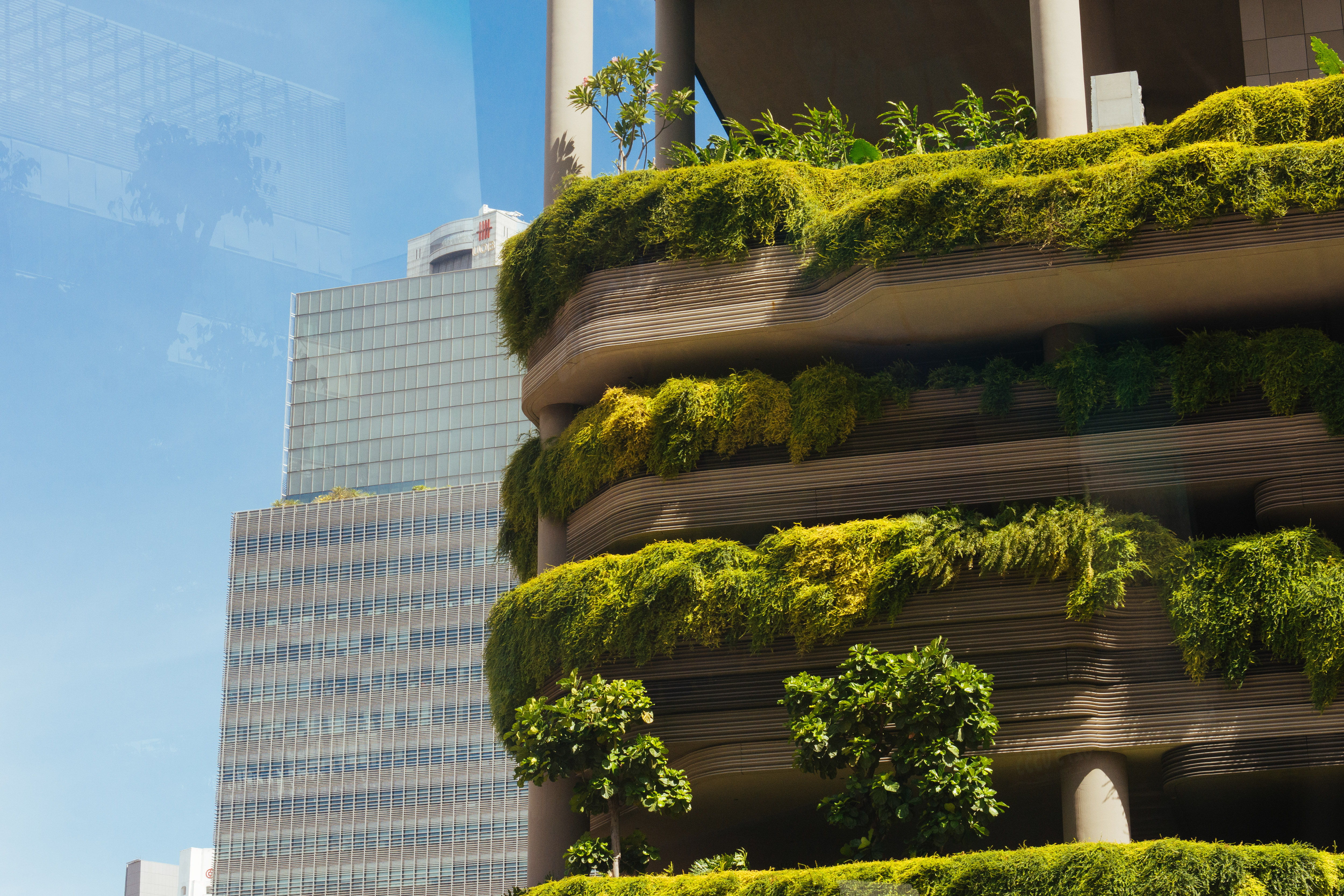 A modern urban building with lush greenery on its balconies, beside a glass skyscraper and blue sky.