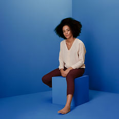 Portrait of a woman sitting on a block in a monochromatic blue room.