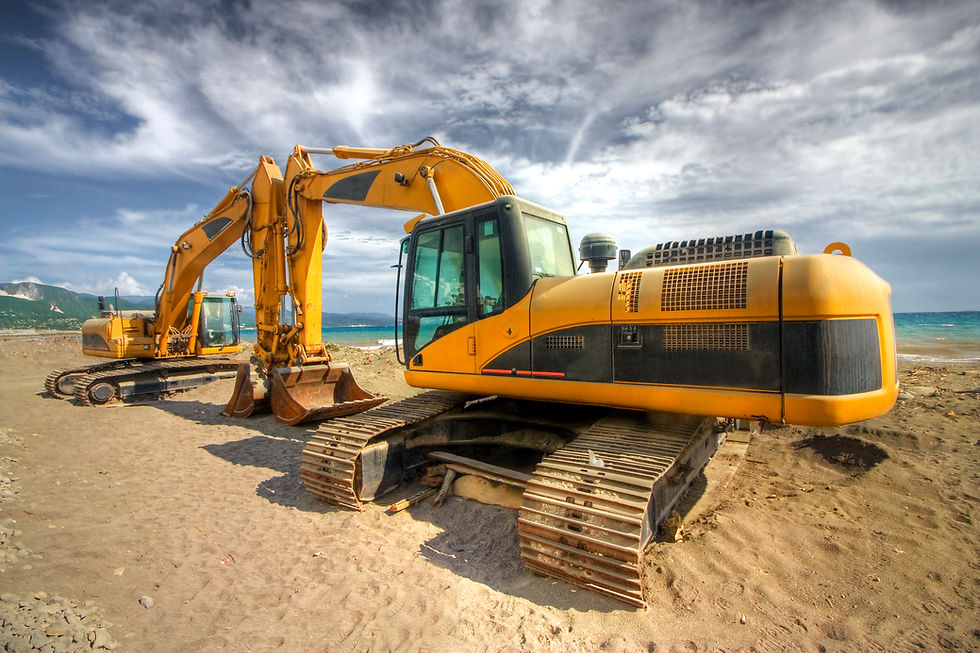 Two yellow hydraulic excavator earth movers parked on a sandy beach with ocean views