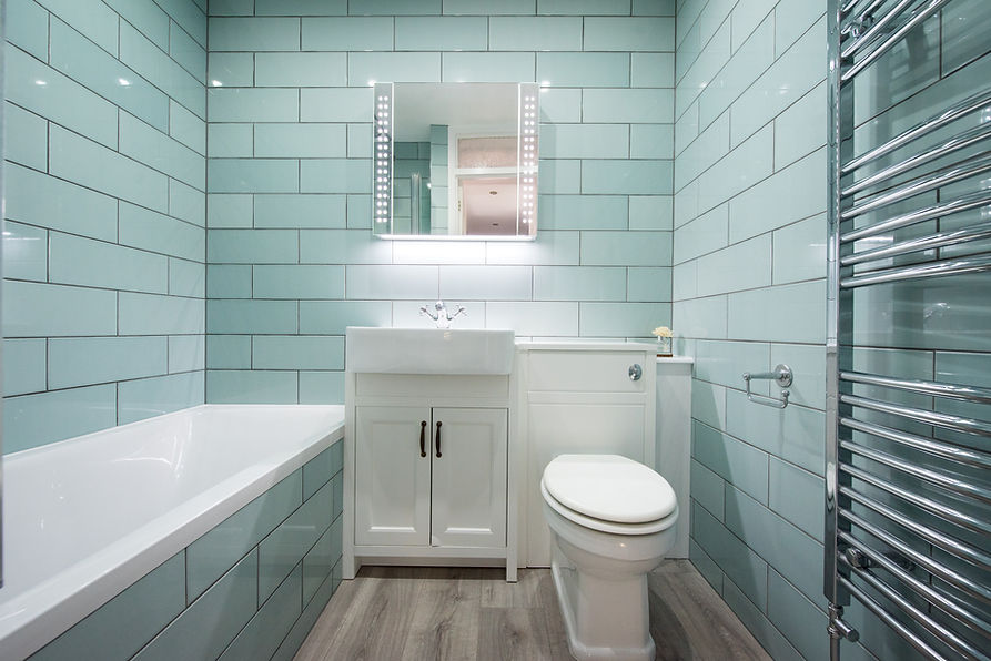 A general interior view of a small bathroom with green rectangular wall tiles, vanity mirr