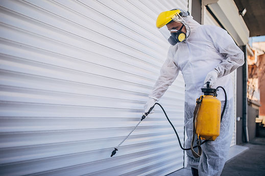 Painter in full protective suit and mask spraying white paint onto a commercial roller shutter door