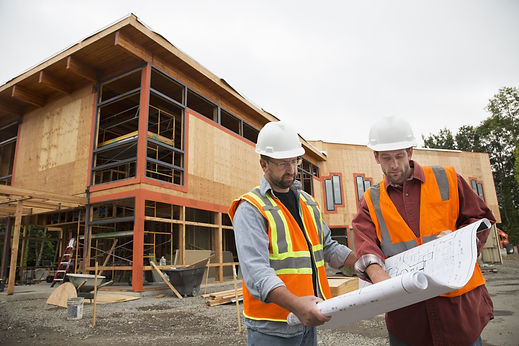Architects in hard hats reviewing building blueprints at timber frame construction site