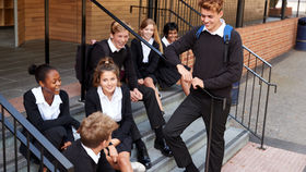 Students in uniforms sitting and chatting on steps outside a building. They appear relaxed and happy, with backpacks and railings visible.