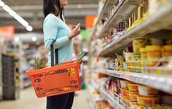 Woman in a grocery aisle with a handheld shopping basket.