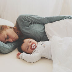 a woman sleeping on a bed with a sleeping baby next to her with a pacifier in it's mouth