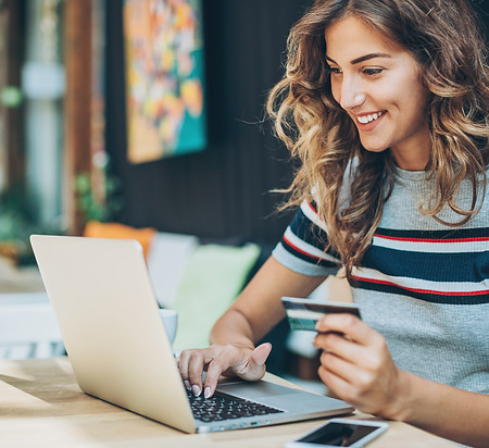 Smiling young woman holding a credit card and typing on a laptop