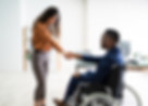 Woman standing giving a handshake to man in a wheelchair.