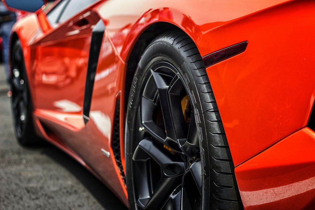 Detail shot of a bright orange sports car's rear wheel and slick tyre