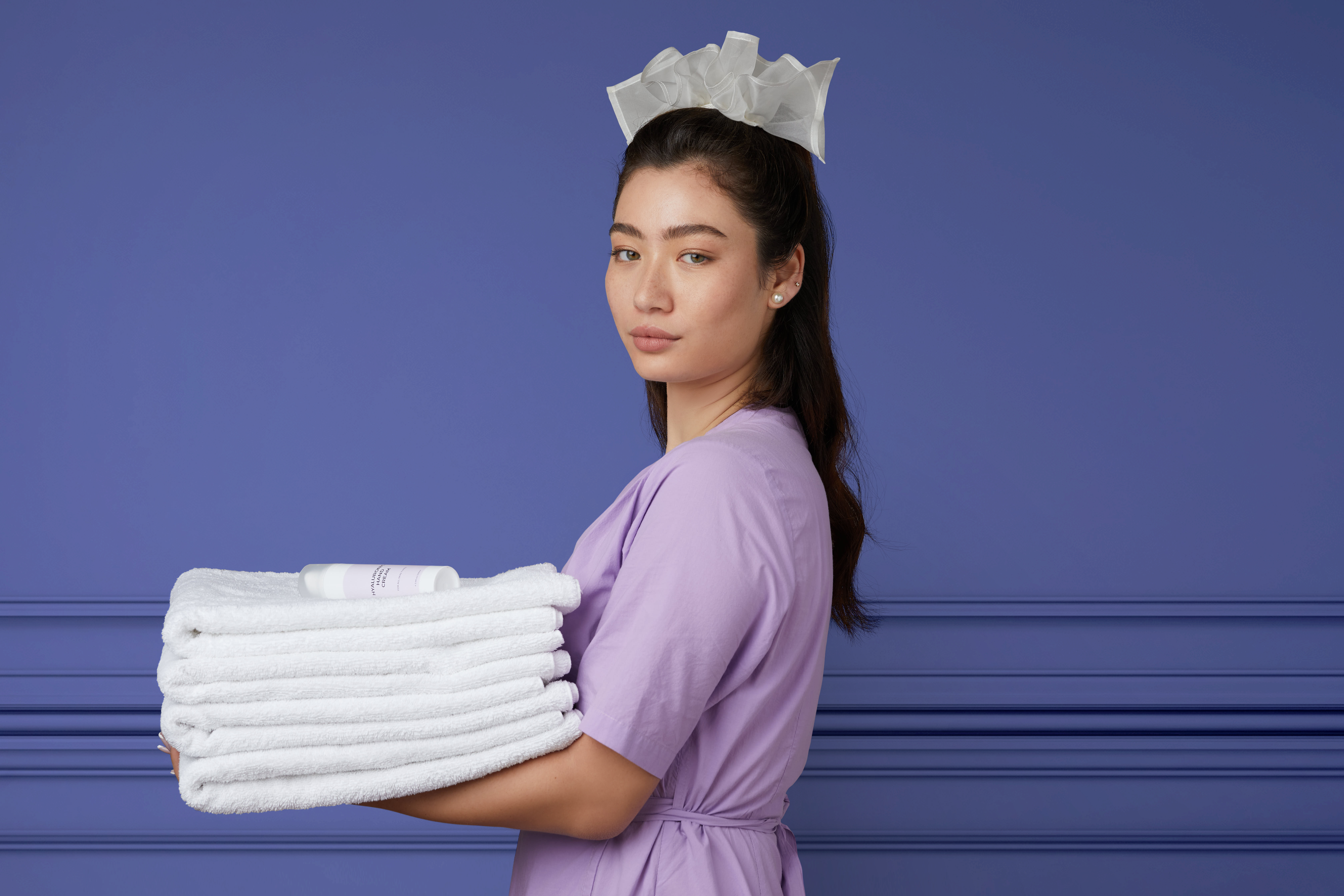 Woman in a purple uniform holding neatly folded white towels standing against a blue background.