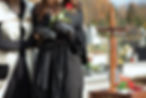 A woman in black attire holds a rose at a cemetery comforted by another person