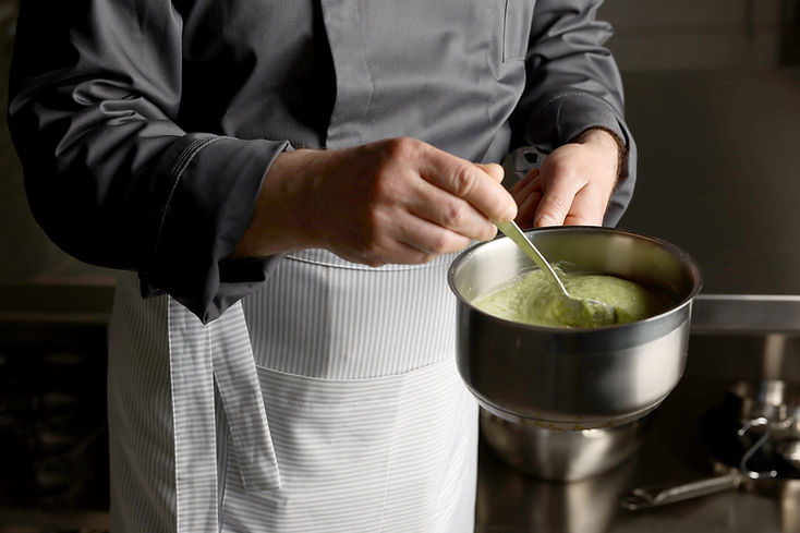 A person in an apron is stirring a sauce in a sauce pan.