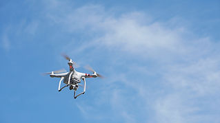 A white quadcopter drone flying against a bright blue sky with thin