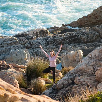 lady in tree pose, in-between rocks, by the ocean