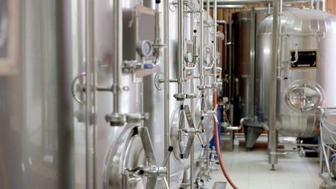 Stainless brewing tanks and piping in a brewery production room
