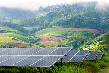 Solar panels in a field with clouds and mountains in the background