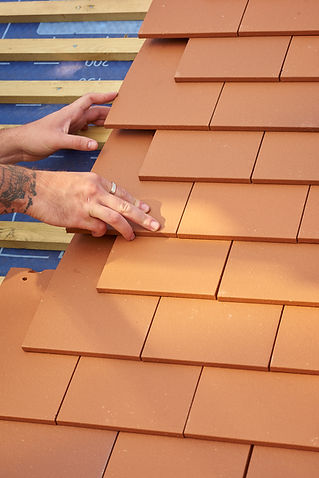 A roofer nails on clay roof tiles