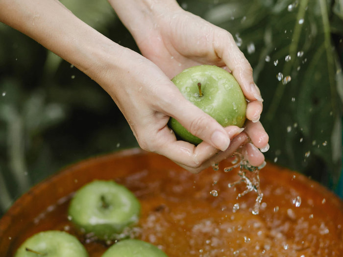 Hands washing green apples in a bowl of water