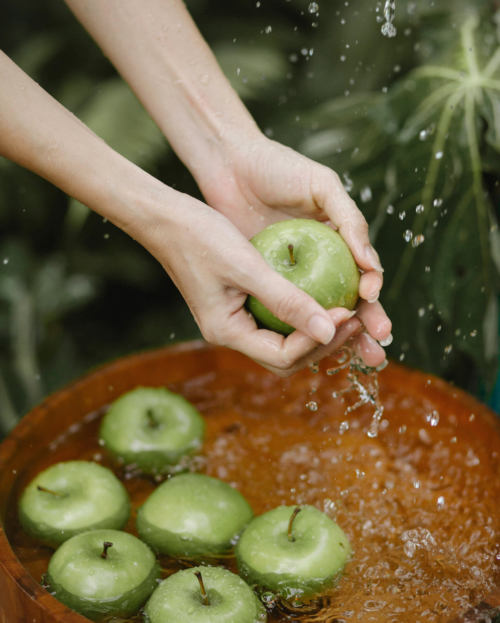 Hands washing green apples in a bowl of water
