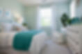 A white bed features teal accents, and a green plant adds a touch of nature.