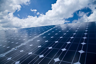 Shiny solar panels angled towards a blue sky with scattered white clouds