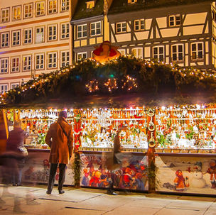 Historic half-timbered houses adorned with festive lights on a cobblestone street at night, creating a warm, vibrant holiday atmosphere.