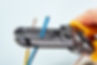 Close-up of an electrician using a yellow wire stripper tool to strip a blue electrical cable