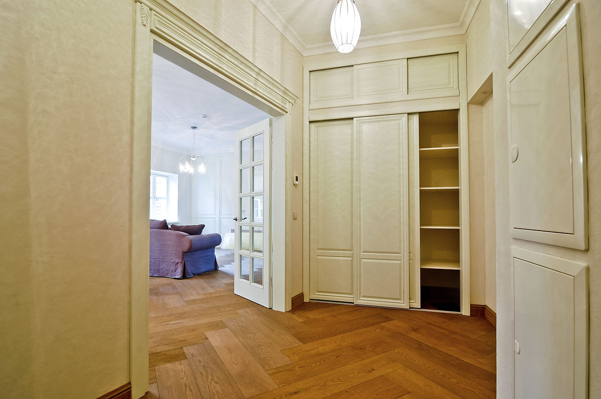 Built-in cream wardrobe with sliding doors and integrated shelving units in a hallway