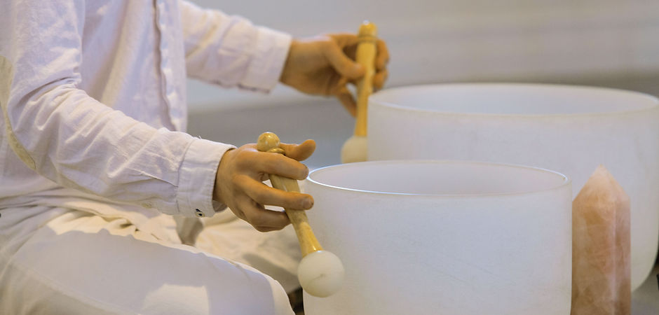 A sound healer gently plays crystal singing bowls in a serene setting, creating soothing vibrations.
