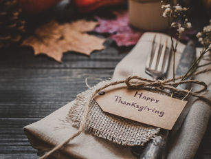 Thanksgiving table setting with a fork and knife on a napkin, adorned with a "Happy Thanksgiving" tag, flowers, and autumn leaves on wood.