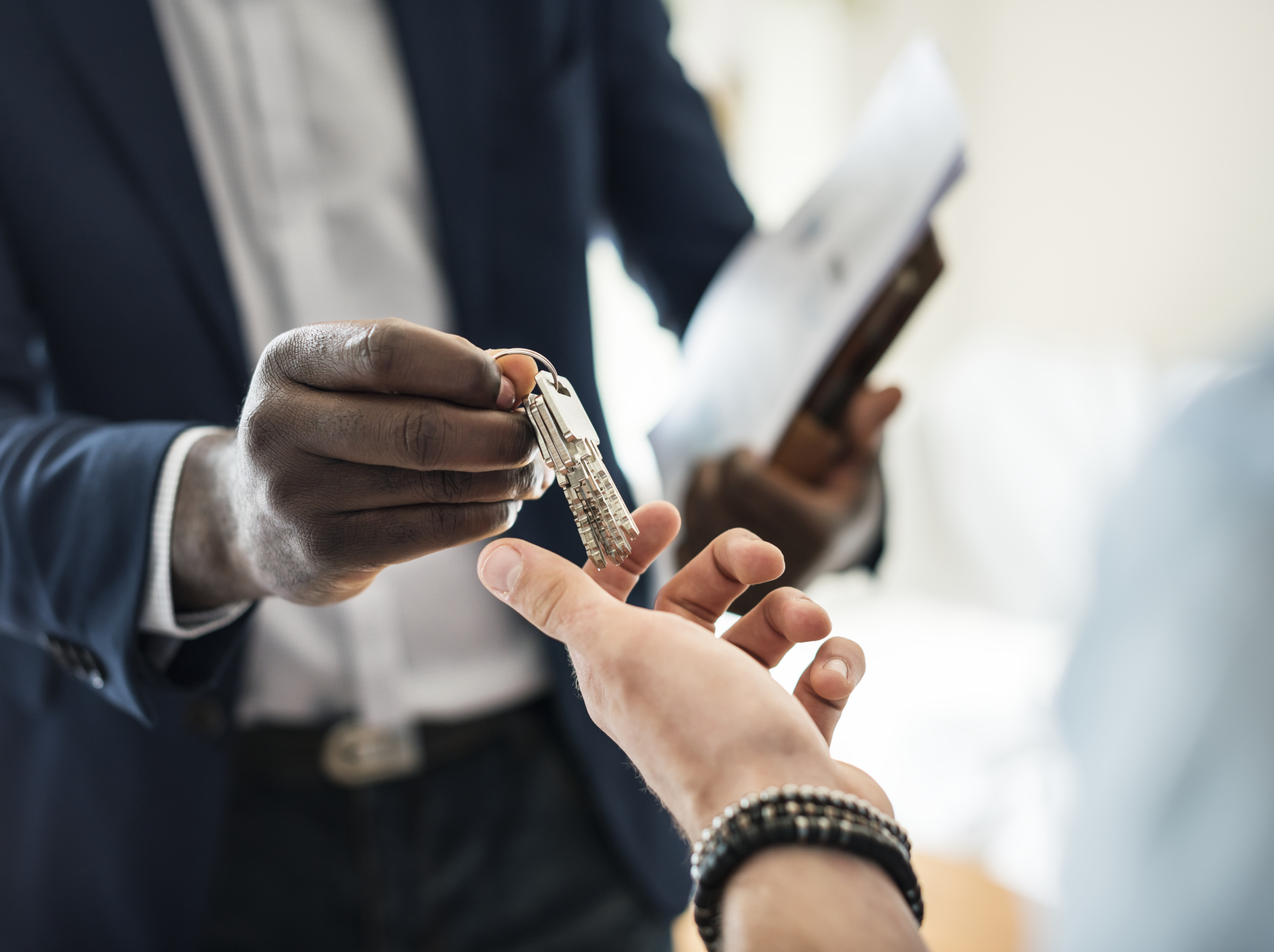 Businessman in a suit hands car keys to another person in a bright office, suggesting a handoff or deal.