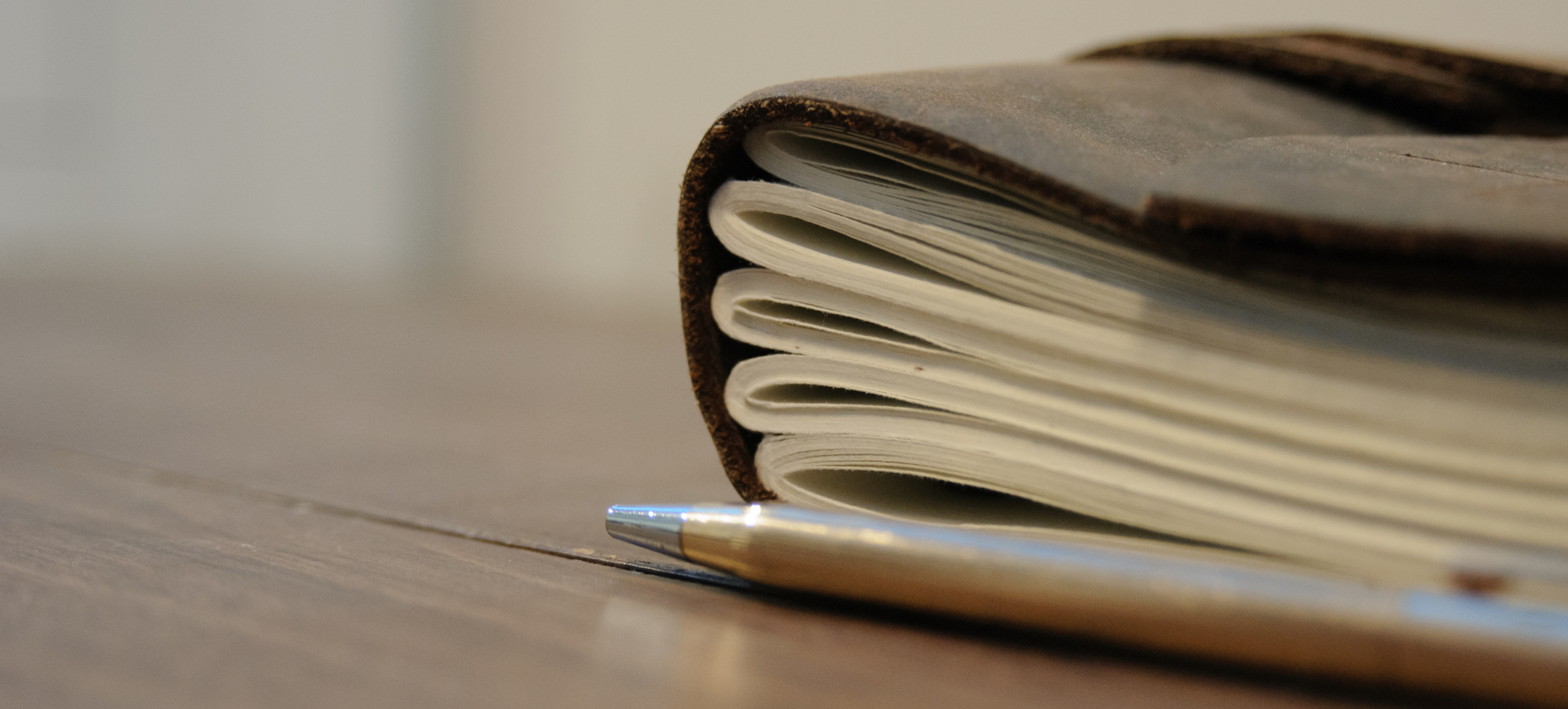 Close-up of a brown notebook and pen on a wooden table, with soft beige background and a calm, minimalist mood