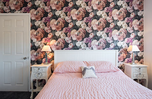 A bedroom with bed, pink roses floral patterned wallpaper,