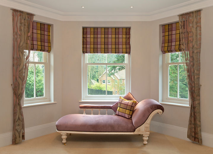 A view of three windows with checked Roman blinds and curtains.