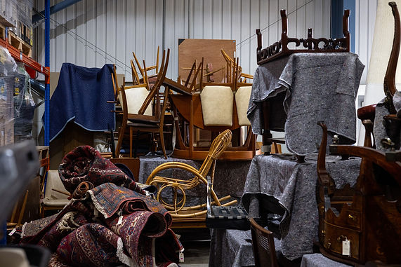 Patterned fabric rugs, wooden chairs, and antique furniture items grouped together inside a storage space