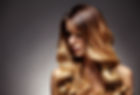 A woman with long, wavy, brown-to-blonde ombre hair gazes downwards